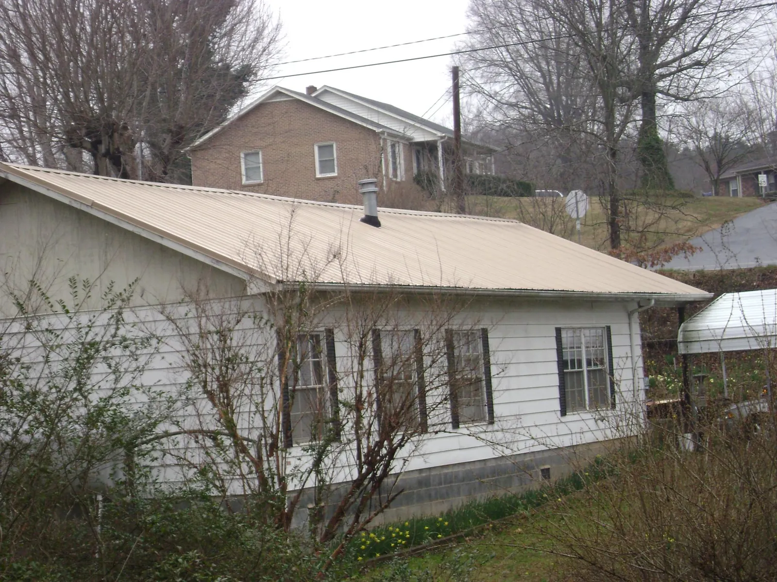 Tan metal roof on a white sided house set into a hillside — Commercial Roofing by Roofing Brothers in Monroeville